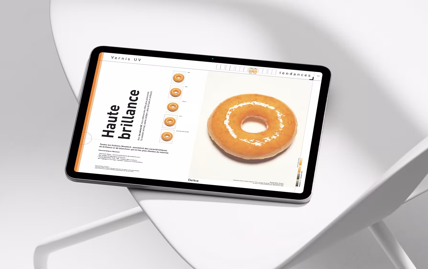 Tablette numérique posée sur une chaise blanche au design contemporain, affichant une page éditoriale sur la brillance et les finitions d’impression.